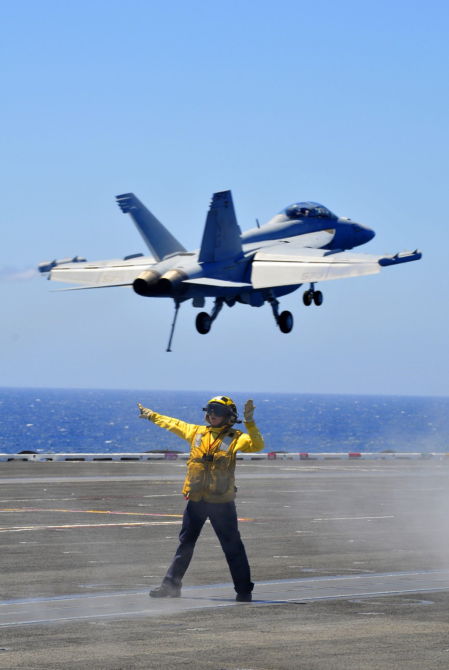 A Sailor in a yellow shirt directs aircraft on the flight deck of USS Carl Vinson.