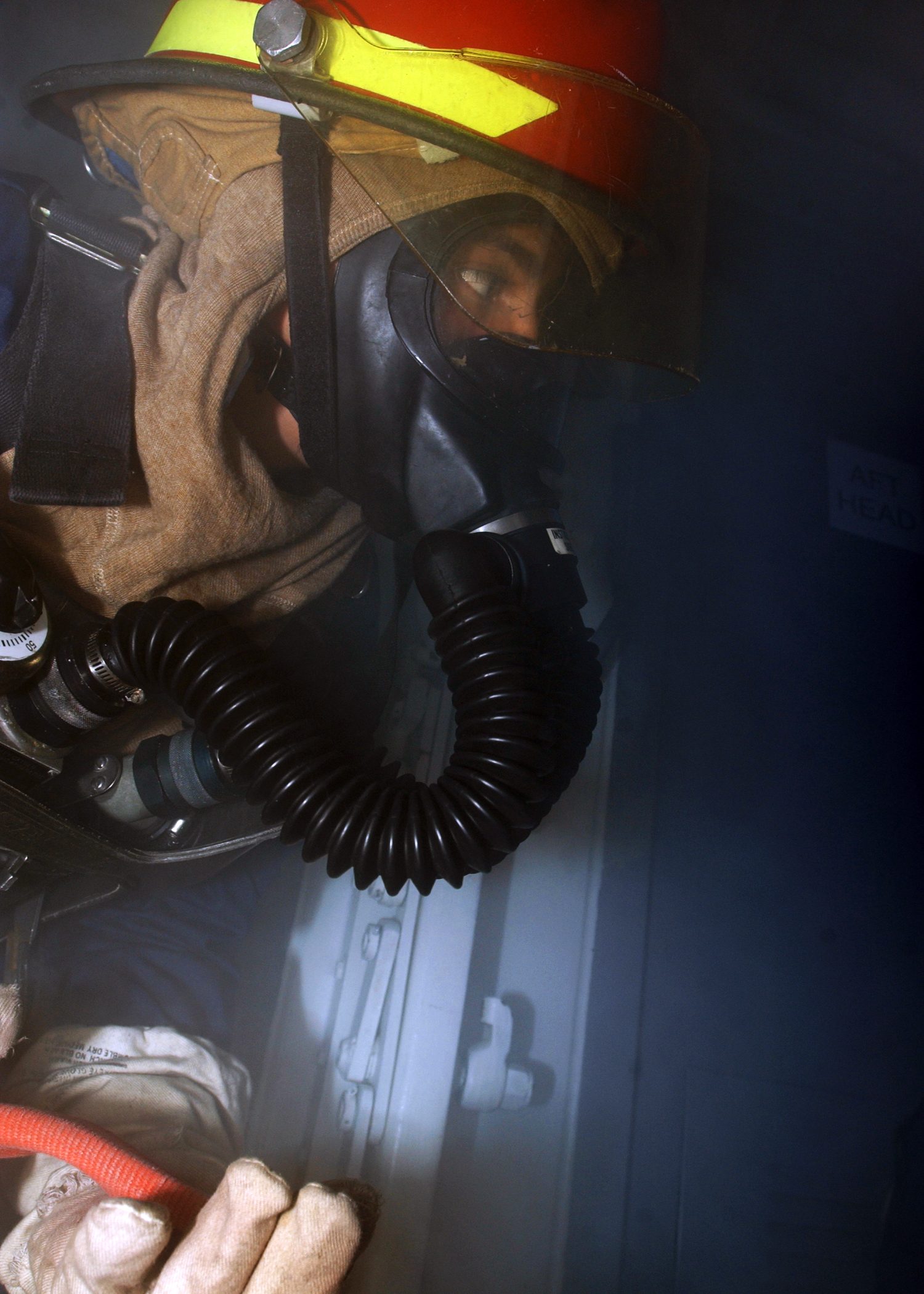 A plebe in firefighting gear enters a smoke-filled compartment during a drill.