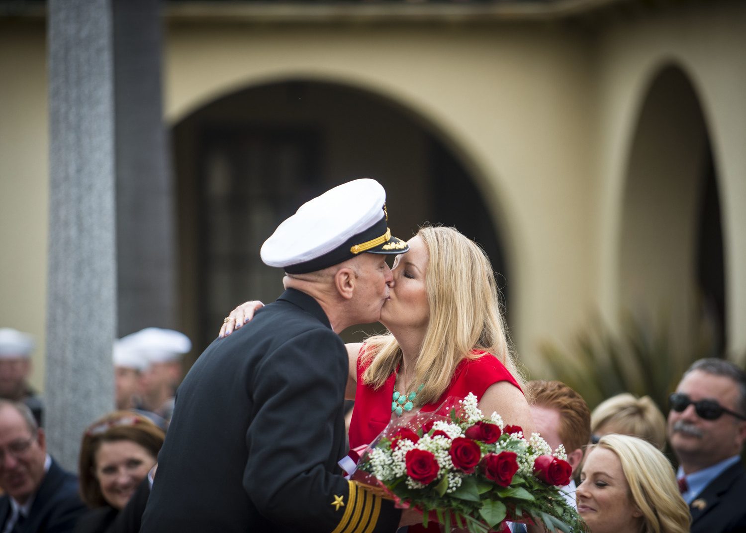 A retiring Navy officer kisses his wife, who holds a bouquet of red roses, at his retirement ceremony.
