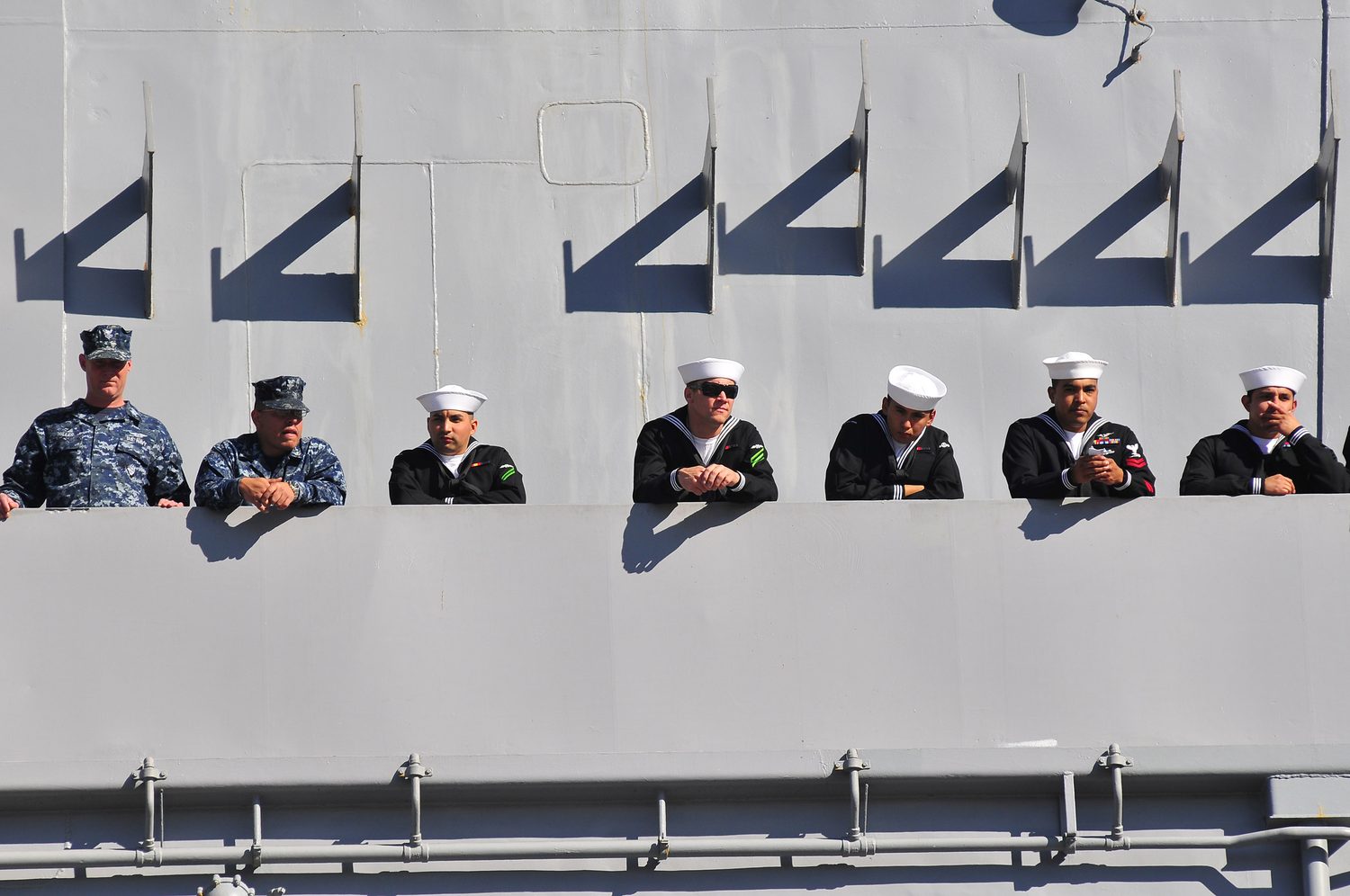 Sailors line the rail of USS Carl Vinson, strong angular shadows across the gray hull.